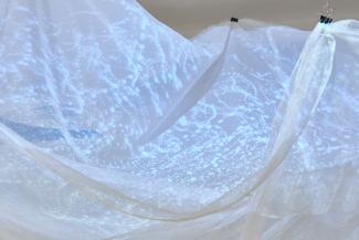 White fabric installation hanging from the ceiling, onto which is projected patterns in blue and red light.