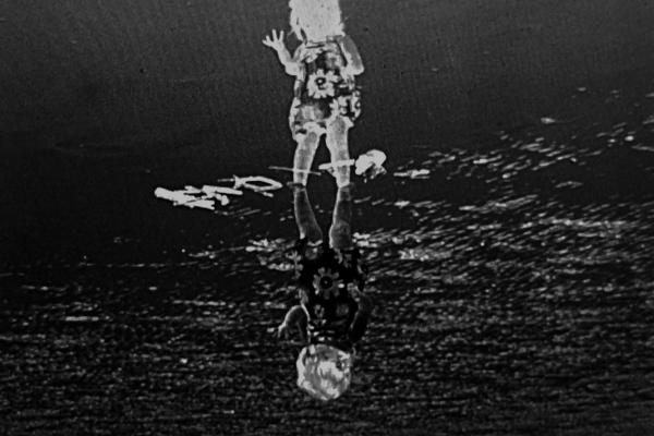 a photographic negative of a child in a floral dress, standing in a black environment with a white textured and reflective round