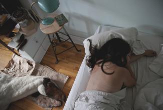 A view from above of a woman laying in bed, with a felt horse on the floor beside her