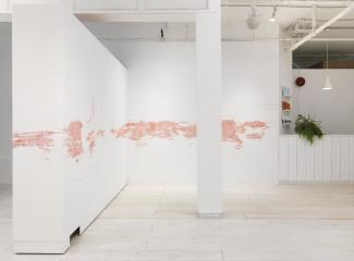 installation view of a long stencilled drawing in pink chalk ending at the administrative desk of the gallery