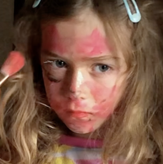 image of a young child's face, appearing serious, covered in red paint, and framed by long hair