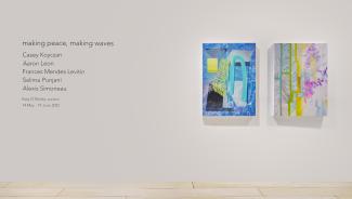 Black vinyl lettering on the left of a wall and two bright paintings on the right. The lettering reads the exhibition title, artists' and curator's names, and exhibition dates. The paintings are abstract in blues, yellows, and pinks.