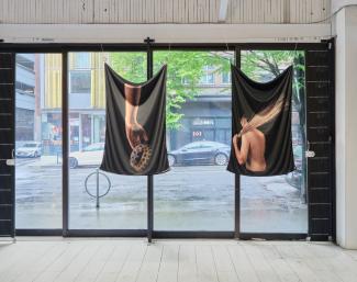 Two photographs printed on fabric hanging in a window. The one on the right is of a hand holding a crown, the other is a figure turned away holding a draw fan over their left shoulder. 