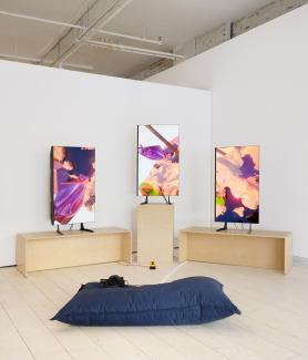​​Art installation with three vibrant digital screens displaying ‘Home404’ by artist Sondi. Wooden benches surround the screens, with a blue cushion and headphones on the floor.