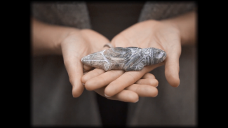 A still from Spirit Emulsion, showing artist Siku Allooloo's hands cradling a small reptile figurine carved from rock. The details are finely etched, with a small divot in the creature's back