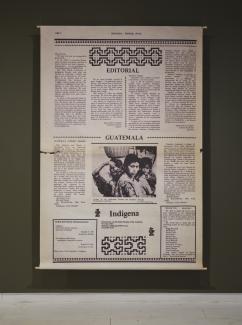 A large canvas prints stretches from floor to ceiling in the gallery. The print shows a newspaper editorial published in Indígena: News From Indian America. 