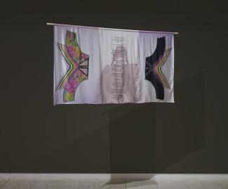 A silk print hangs in the gallery, bordered on each side by photographic images of a beaded chest piece. In the centre, a poem is overlaid on a black and white photo of the artist's grandmother. She is a young girl in the photo, wearing an amauti (parka) with long dark braids.